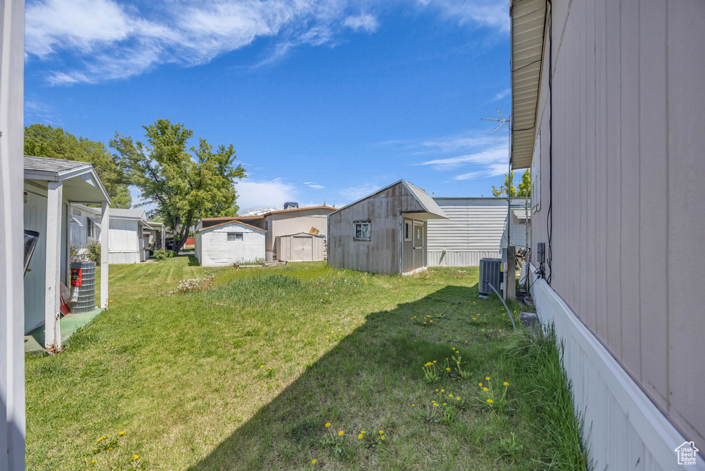 View of green lawn with a shed, an outdoor structure, and central air condition unit