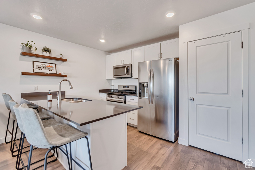 Kitchen with appliances with stainless steel finishes, a sink, a kitchen breakfast bar, open shelves, and white cabinets
