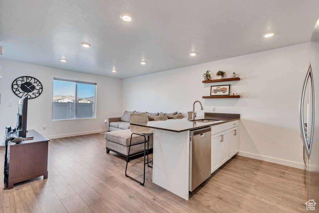 Kitchen featuring a sink, appliances with stainless steel finishes, open floor plan, a peninsula, and light wood-style floors
