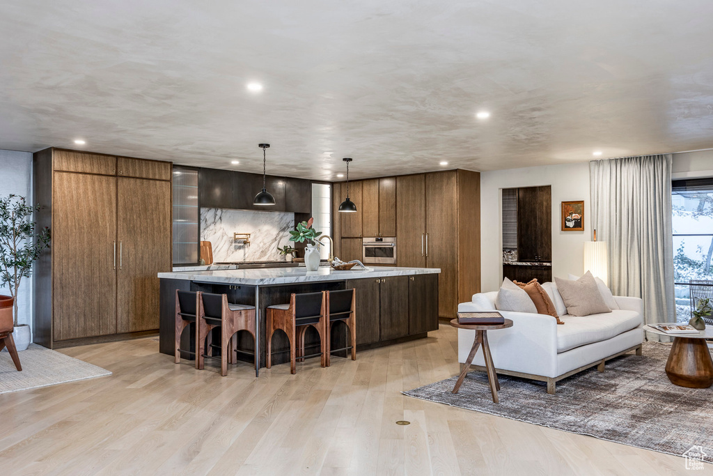 Kitchen featuring stainless steel oven, a spacious island, light wood-style floors, recessed lighting, and a kitchen bar