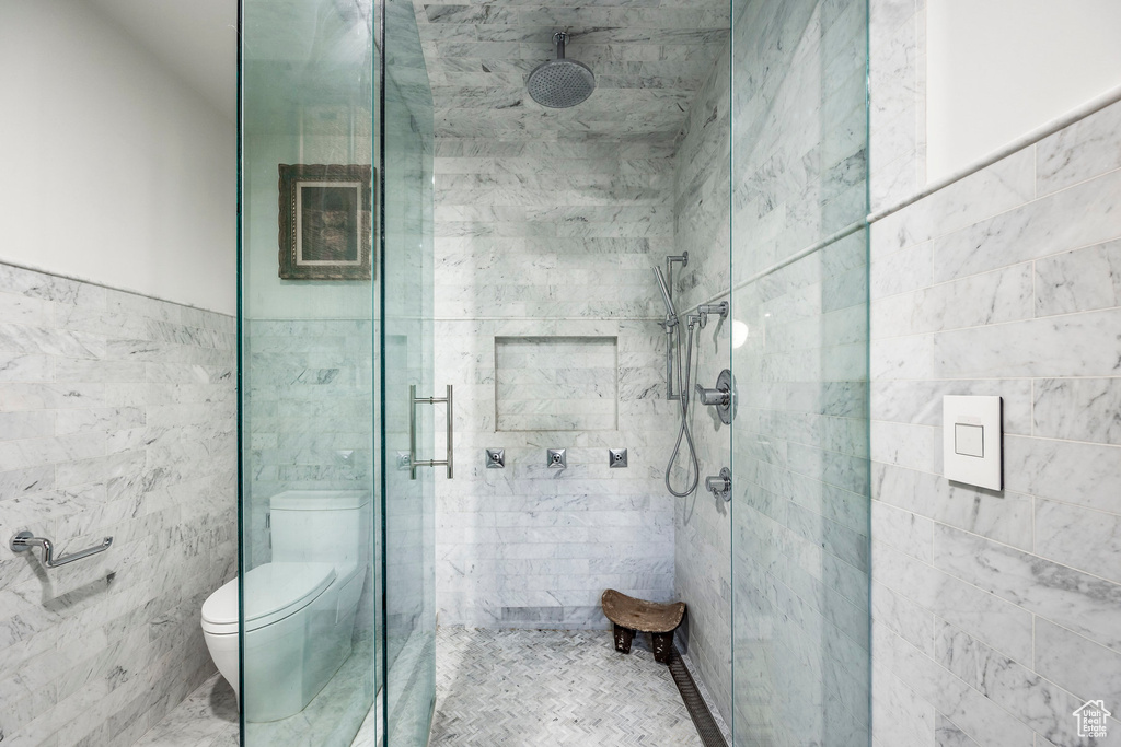 Bathroom with tile walls, a shower stall, and toilet
