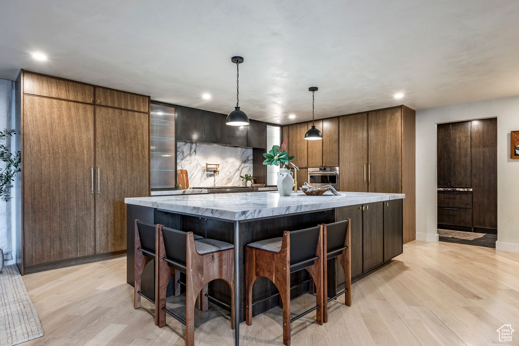 Kitchen with stainless steel oven, light wood-style flooring, a spacious island, recessed lighting, and light stone counters