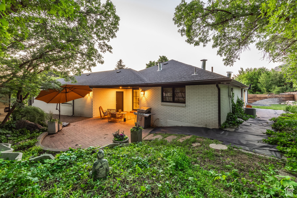 Rear view of property with brick siding, a patio area, and roof with shingles