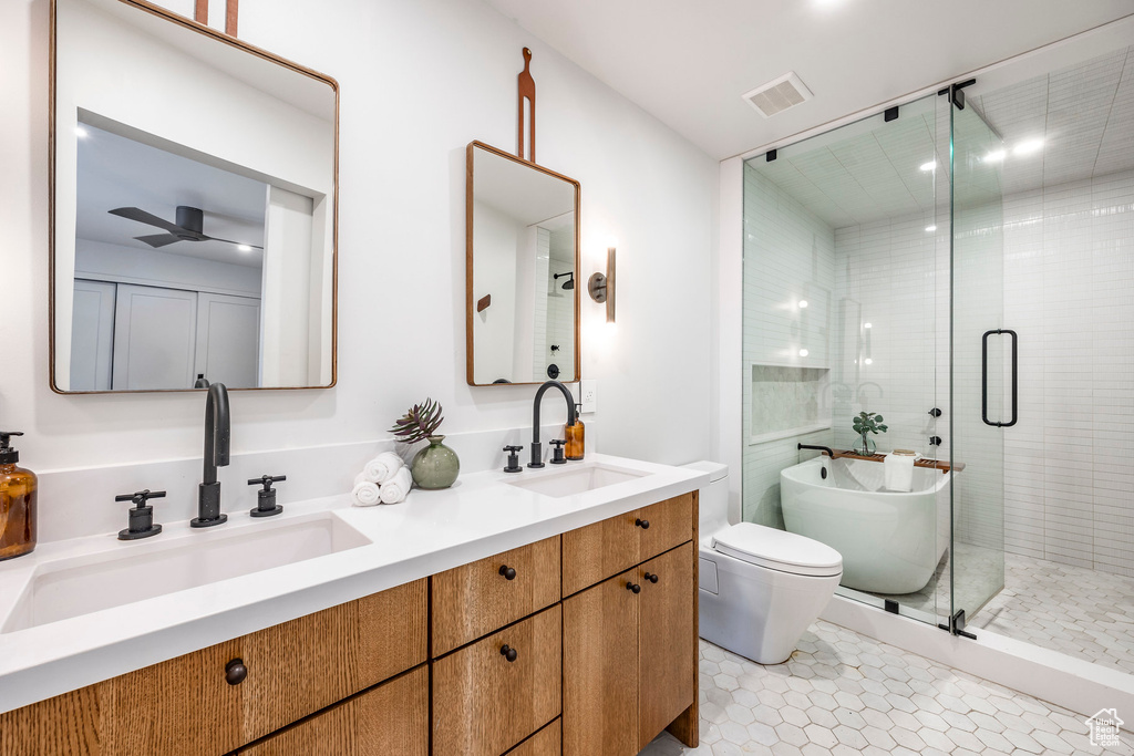 Bathroom featuring a stall shower, a ceiling fan, double vanity, a soaking tub, and toilet