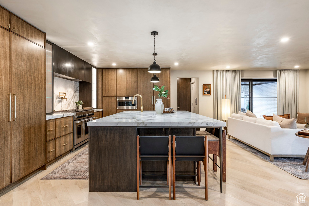 Kitchen featuring appliances with stainless steel finishes, modern cabinets, a breakfast bar area, a large island, and light wood-type flooring