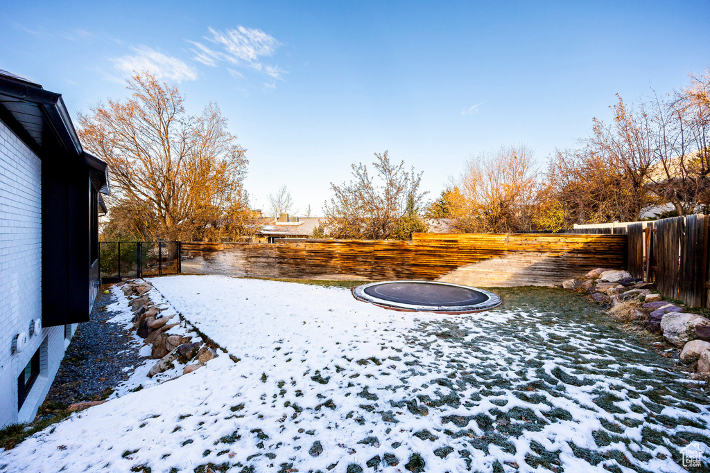 Snowy yard featuring a trampoline and a fenced backyard