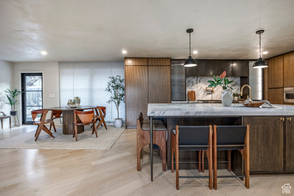 Kitchen featuring stainless steel oven, a breakfast bar, light wood-style flooring, hanging light fixtures, and recessed lighting