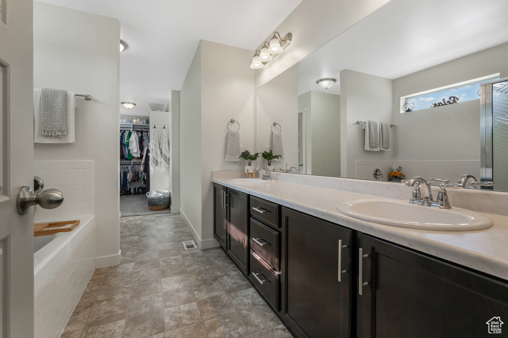 Full bath with double vanity, a walk in closet, and a tub