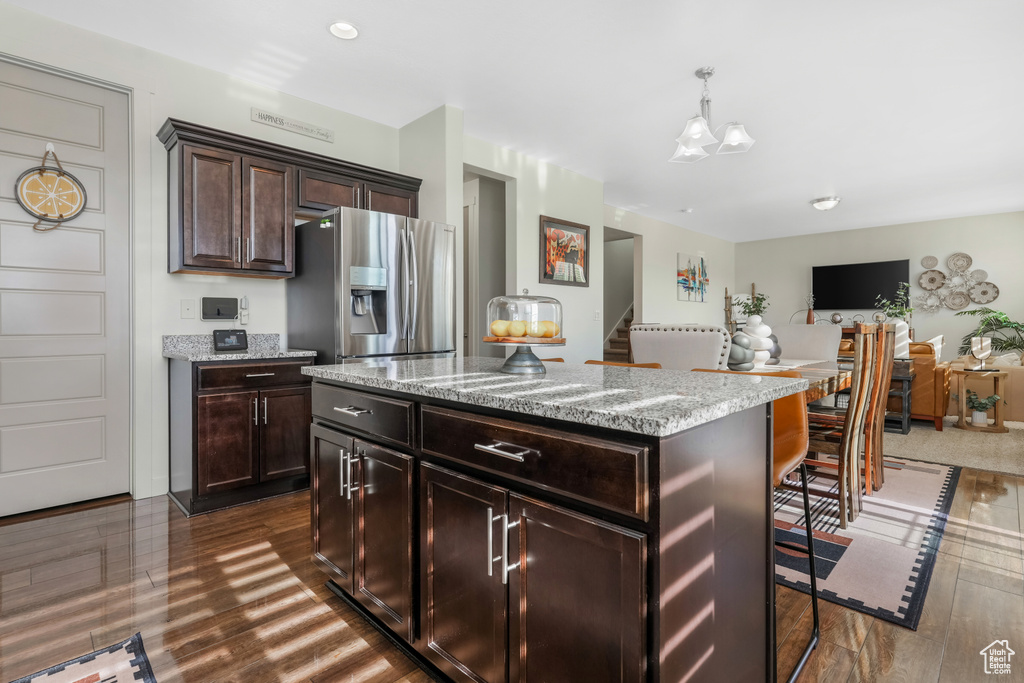 Kitchen featuring stainless steel refrigerator with ice dispenser, dark wood-type flooring, light stone counters, and dark brown cabinetry