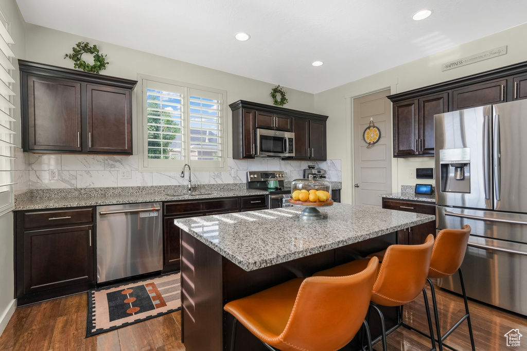 Kitchen featuring appliances with stainless steel finishes, a sink, a center island, tasteful backsplash, and dark brown cabinetry