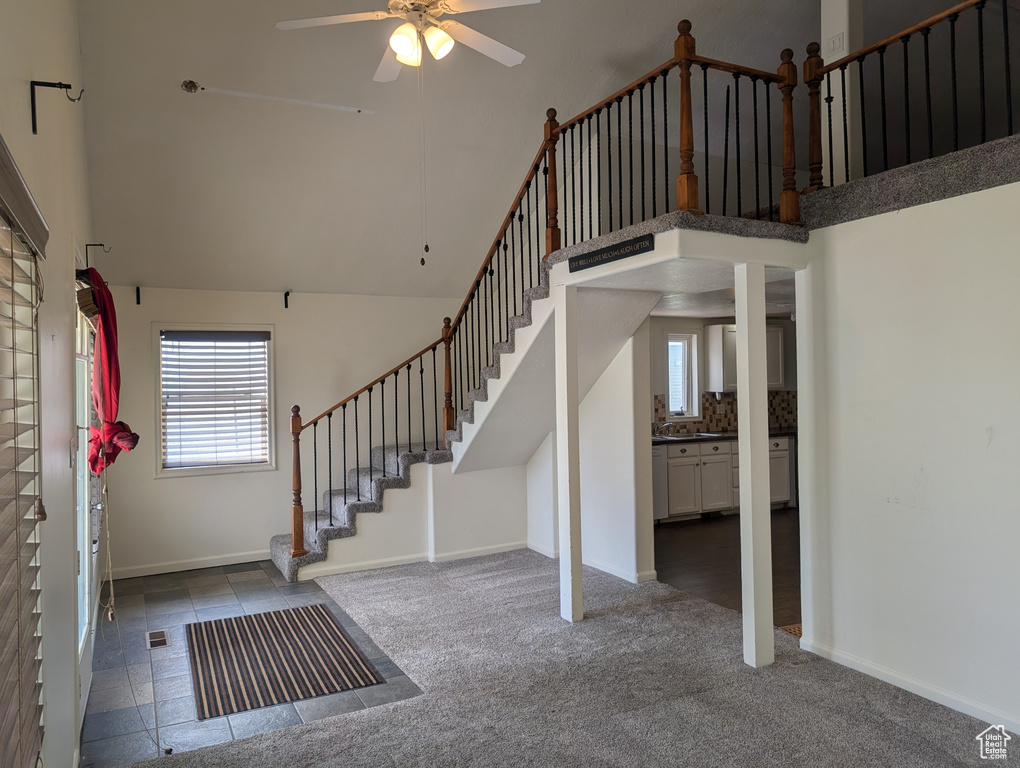 Stairway with ceiling fan, a towering ceiling, baseboards, and carpet flooring