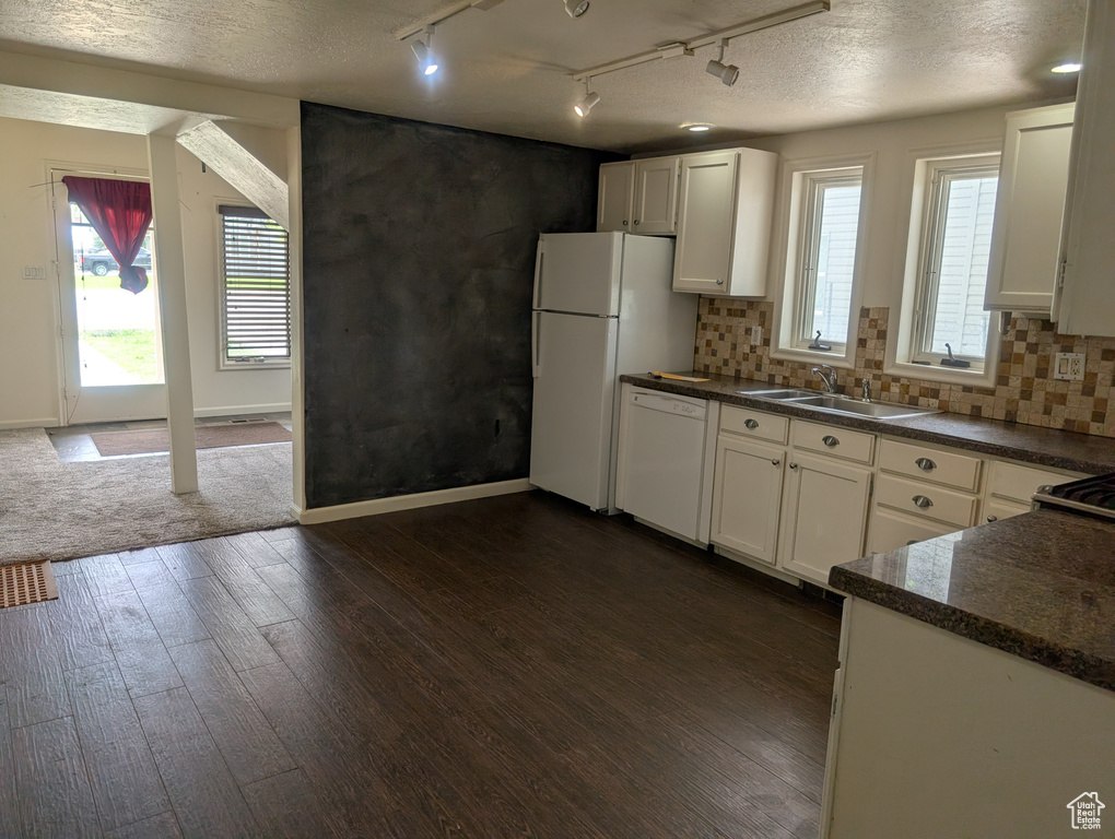 Kitchen featuring white appliances, a sink, rail lighting, dark countertops, and dark wood-type flooring