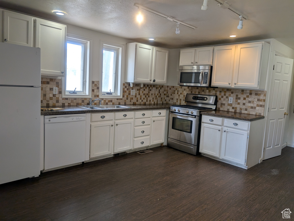 Kitchen with stainless steel appliances, a sink, dark countertops, white cabinets, and dark wood-type flooring