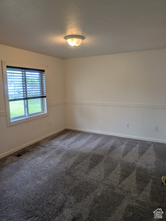 Empty room with dark colored carpet, a textured ceiling, baseboards, and wainscoting
