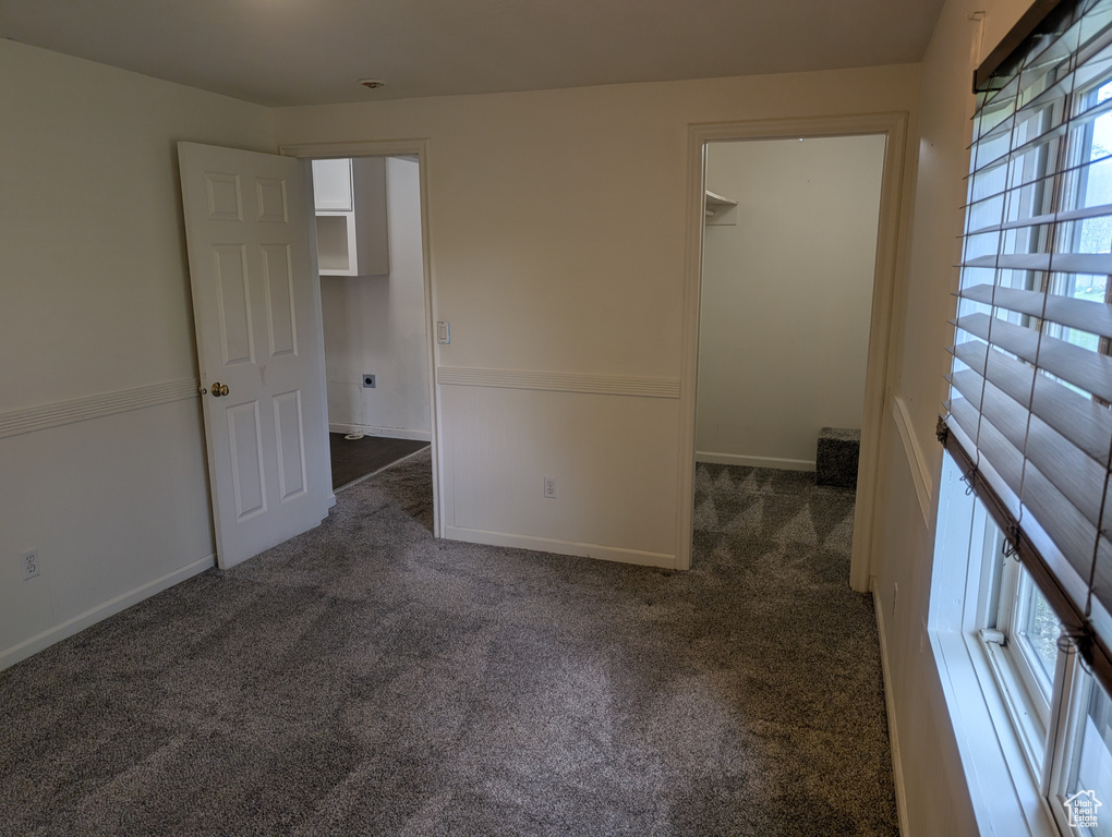 Unfurnished bedroom with dark carpet, a spacious closet, and baseboards