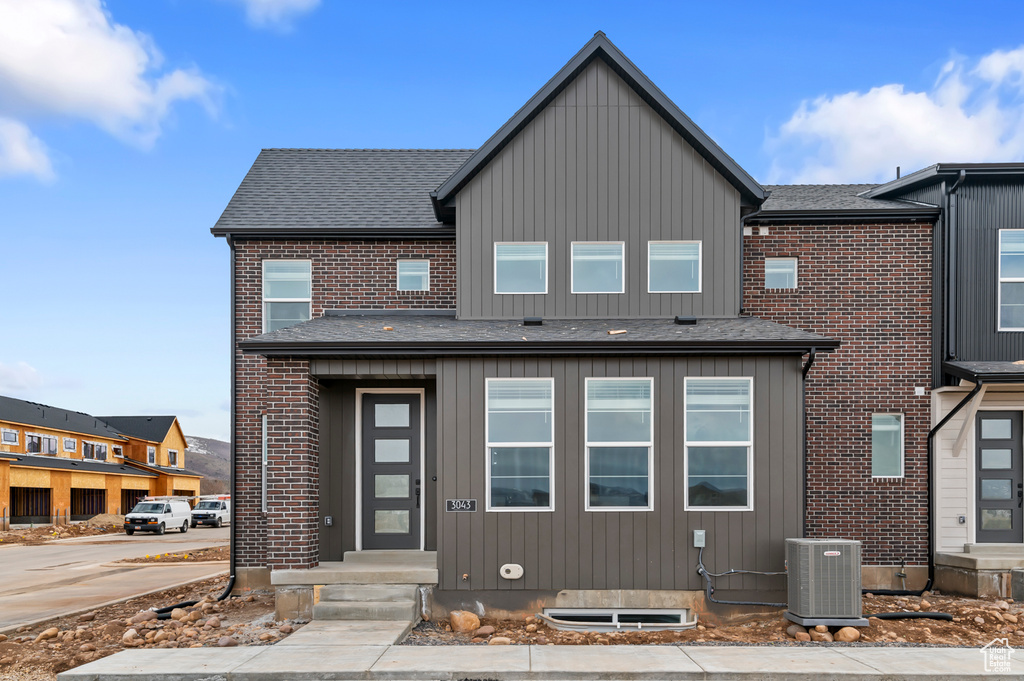 View of front of house with central AC unit, roof with shingles, and brick siding