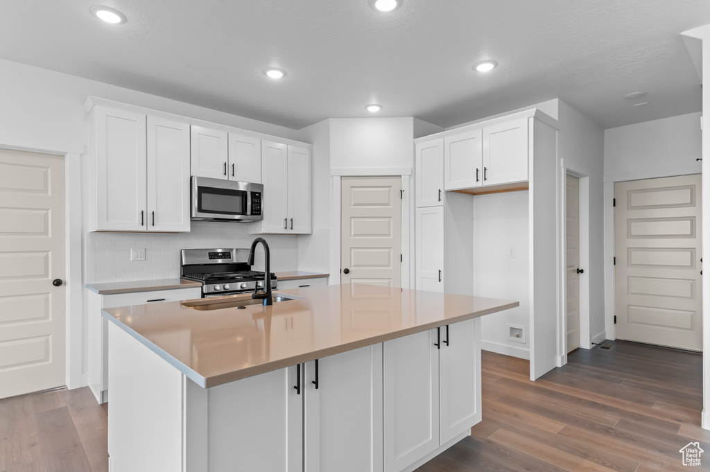 Kitchen with stainless steel appliances, a sink, wood finished floors, white cabinetry, and a center island with sink