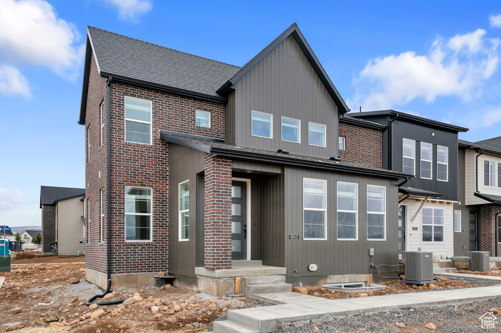 View of front of home featuring central AC, brick siding, and roof with shingles