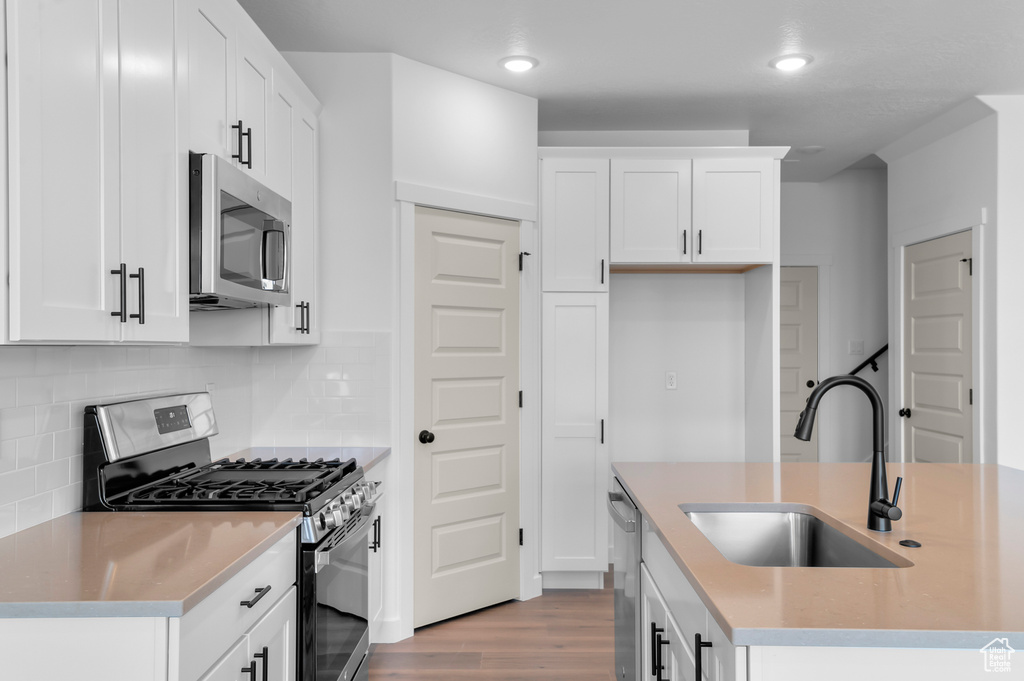 Kitchen featuring stainless steel appliances, a sink, wood finished floors, white cabinets, and recessed lighting
