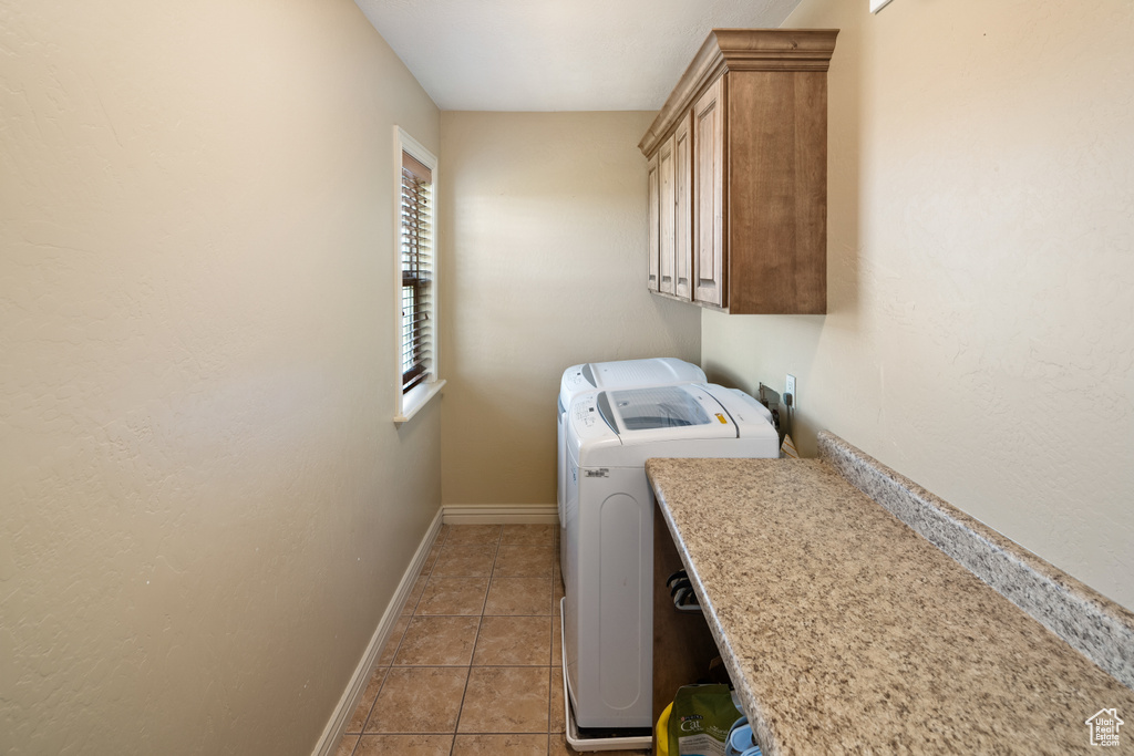 Washroom featuring washer and clothes dryer, light tile patterned floors, baseboards, and cabinet space