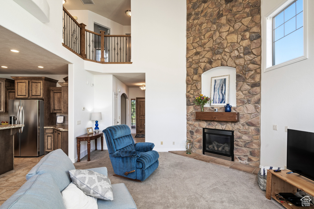 Living room featuring healthy amount of natural light, a stone fireplace, a high ceiling, light colored carpet, and recessed lighting