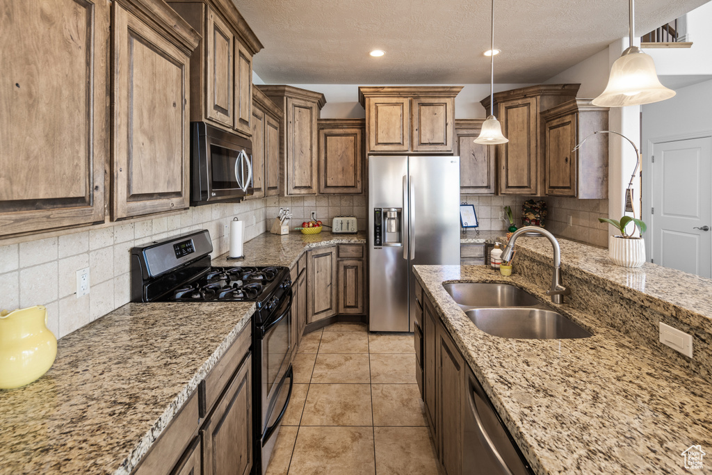 Kitchen featuring stainless steel appliances, a sink, tasteful backsplash, light stone countertops, and a textured ceiling