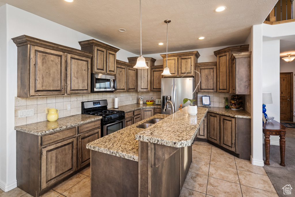 Kitchen featuring appliances with stainless steel finishes, a sink, a center island with sink, recessed lighting, and tasteful backsplash