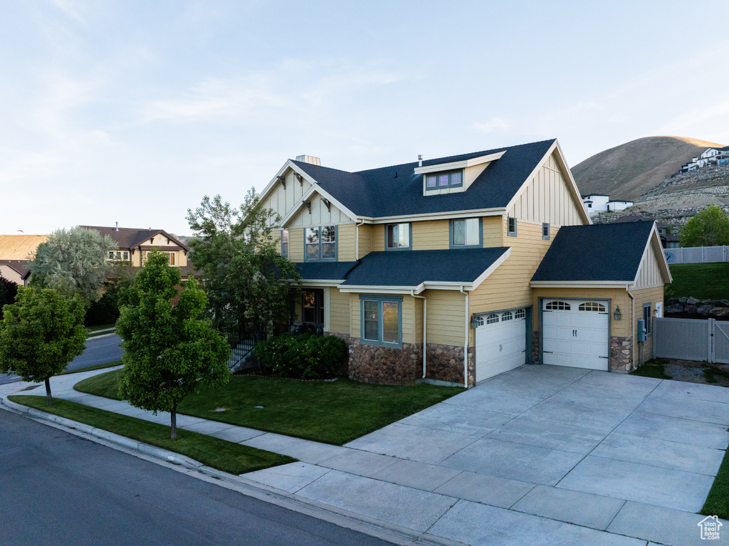 View of front facade with board and batten siding, stone siding, concrete driveway, a gate, and a garage