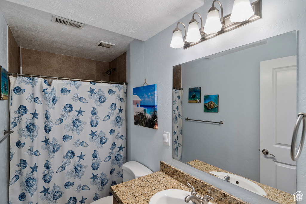 Full bath featuring a textured ceiling, vanity, a shower with shower curtain, and toilet
