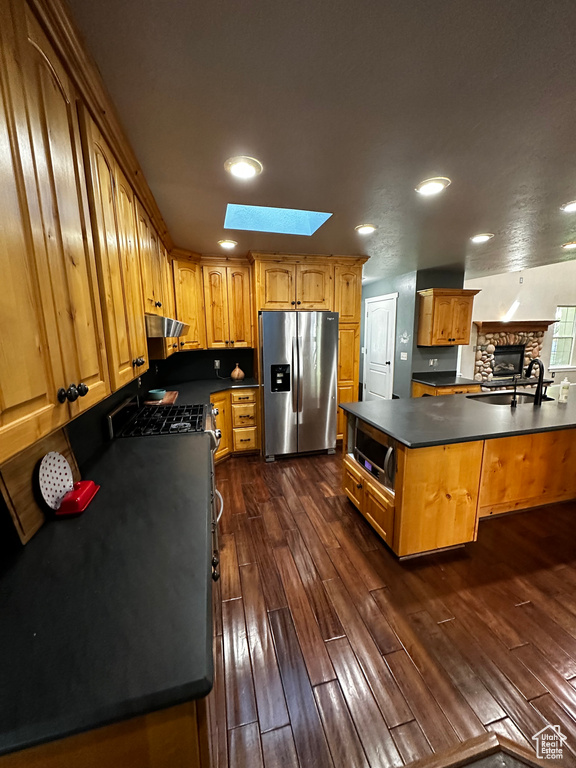 Kitchen featuring stainless steel appliances, dark countertops, a skylight, dark wood-type flooring, and recessed lighting