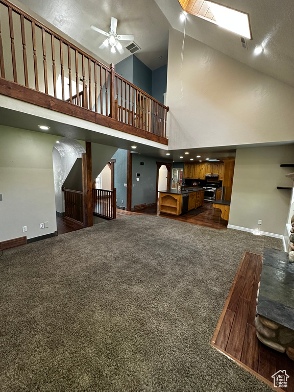 Unfurnished living room featuring dark carpet, a towering ceiling, baseboards, ceiling fan, and stairway