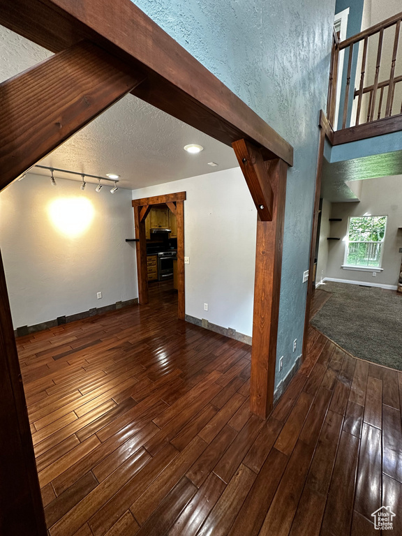 Unfurnished living room featuring hardwood / wood-style floors, baseboards, track lighting, and a textured ceiling