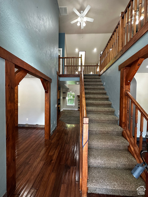 Stairs with ceiling fan, wood-type flooring, and a high ceiling