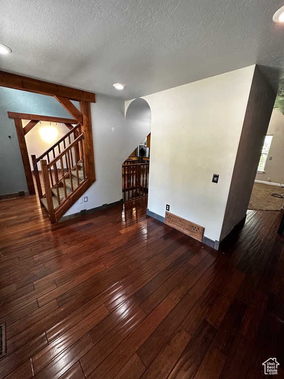 Unfurnished living room with arched walkways, stairway, hardwood / wood-style flooring, a textured ceiling, and baseboards