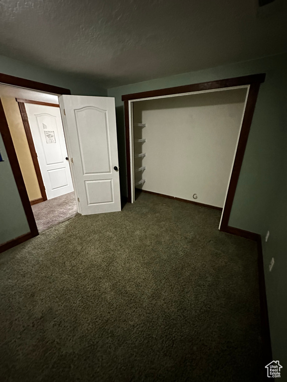 Unfurnished bedroom featuring a textured ceiling, dark carpet, and baseboards