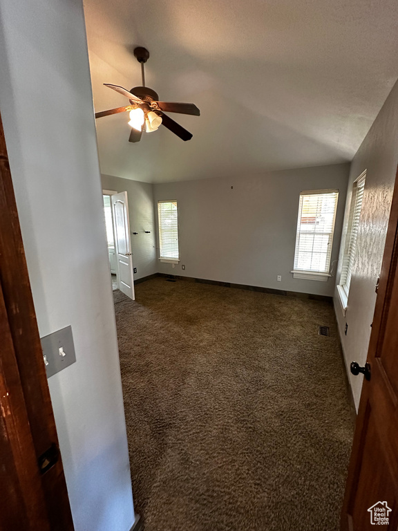 Spare room featuring dark carpet, a ceiling fan, baseboards, and vaulted ceiling