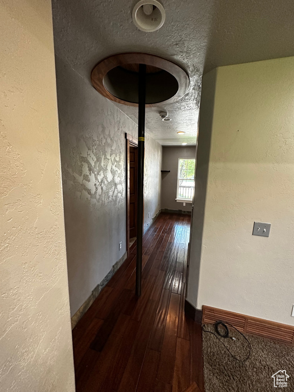 Hall with dark wood-style flooring, baseboards, and a textured wall