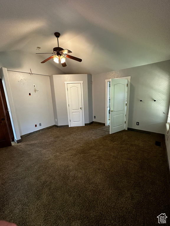 Unfurnished bedroom with dark colored carpet, lofted ceiling, baseboards, and a ceiling fan