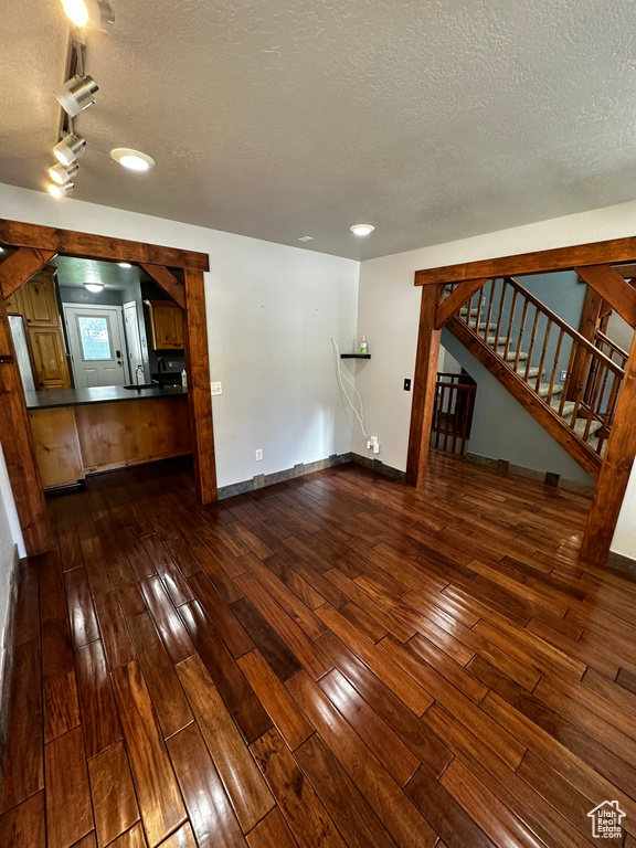 Unfurnished living room with dark wood-style flooring, stairway, a textured ceiling, baseboards, and recessed lighting