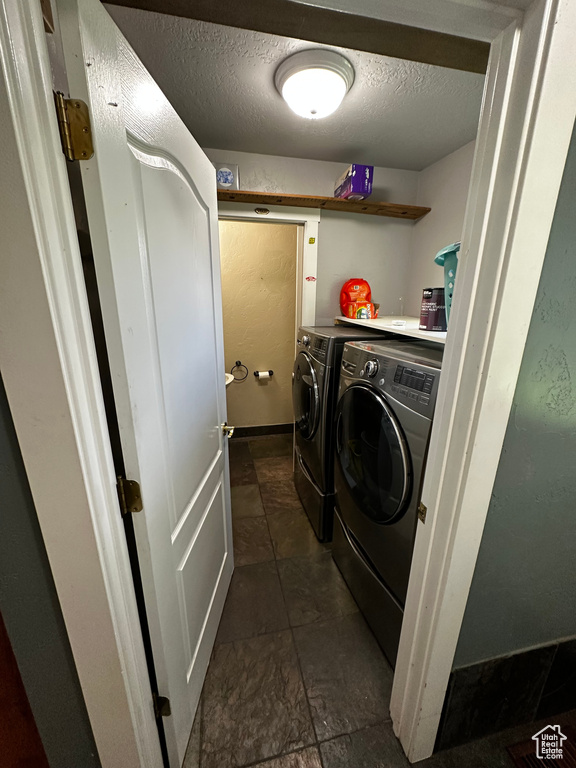 Washroom with washing machine and dryer, a textured ceiling, and baseboards