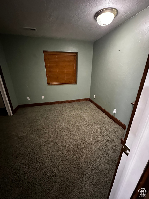 Empty room featuring a textured ceiling, dark colored carpet, and baseboards