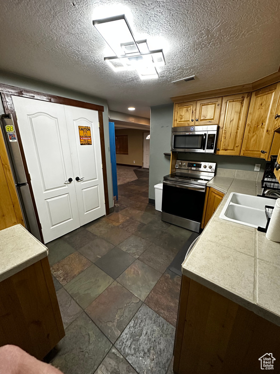 Kitchen featuring stainless steel appliances, a sink, light countertops, dark stone finish flooring, and a textured ceiling