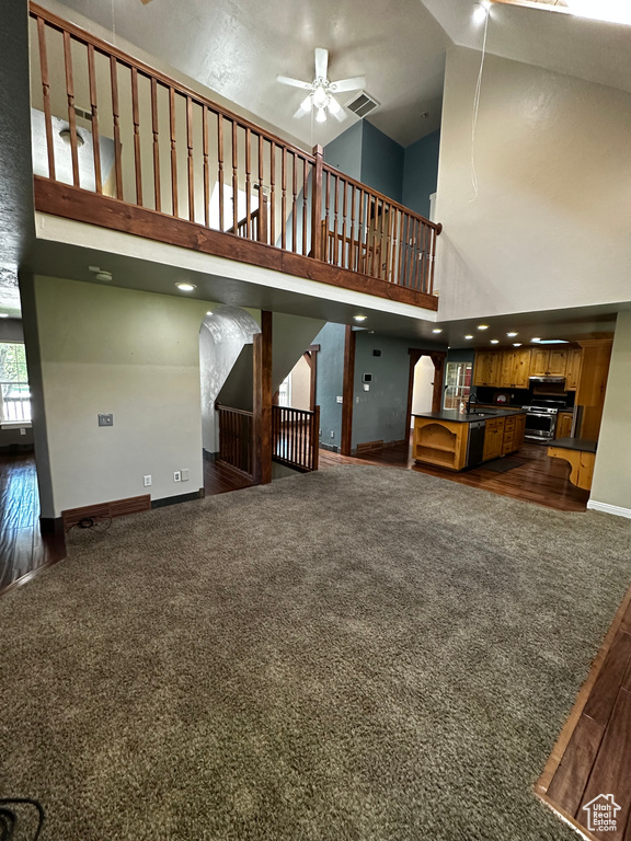 Unfurnished living room with a high ceiling, dark colored carpet, ceiling fan, baseboards, and stairway