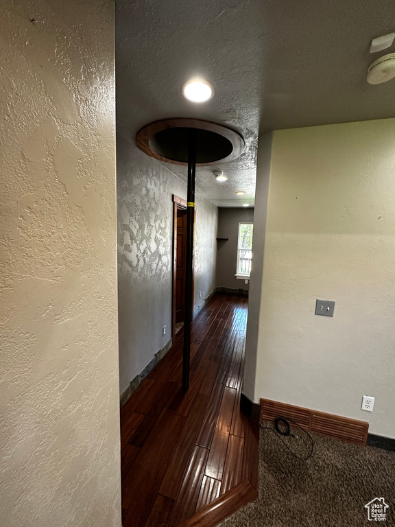Corridor featuring a textured wall, baseboards, hardwood / wood-style floors, and a textured ceiling