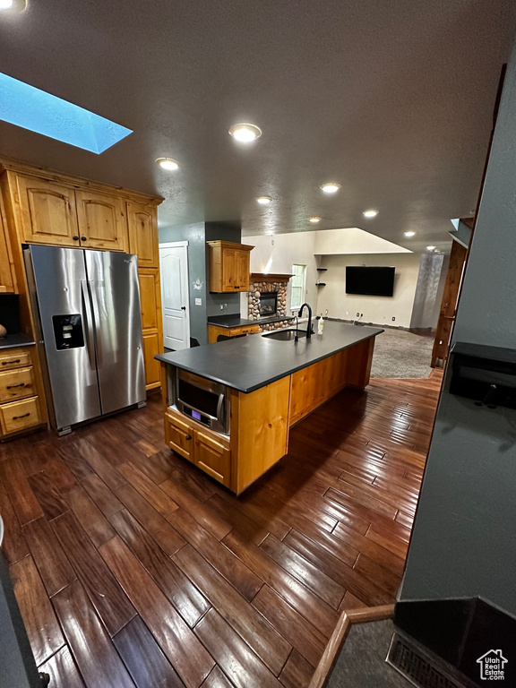 Kitchen with appliances with stainless steel finishes, a skylight, open floor plan, dark countertops, and a sink