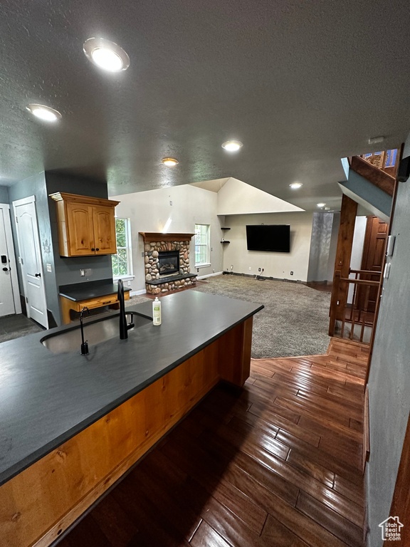 Kitchen featuring a textured ceiling, dark countertops, open floor plan, dark wood-style floors, and a fireplace