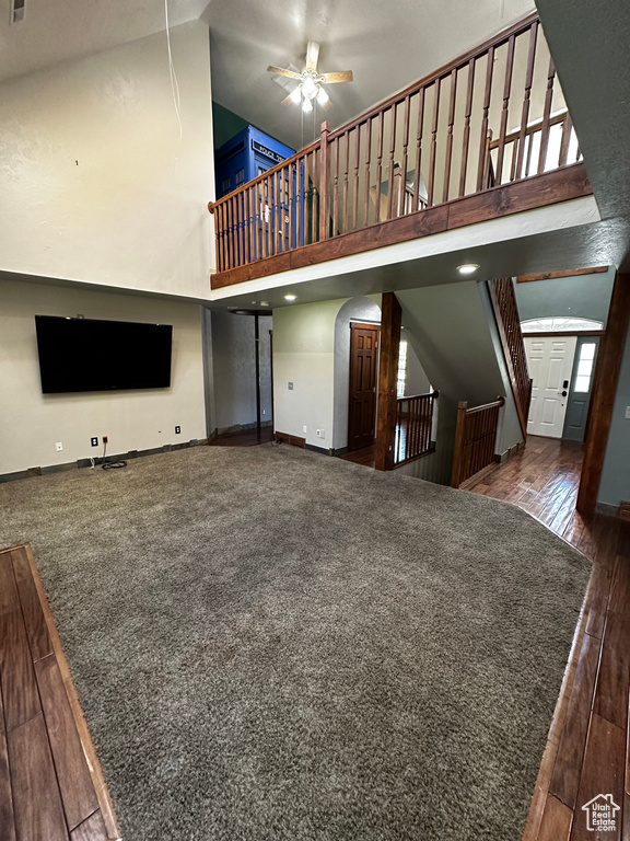 Unfurnished living room featuring high vaulted ceiling, baseboards, wood finished floors, ceiling fan, and stairs