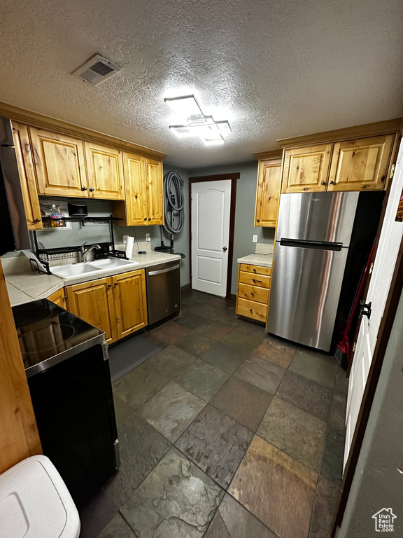 Kitchen featuring appliances with stainless steel finishes, a sink, dark stone finish flooring, and a textured ceiling