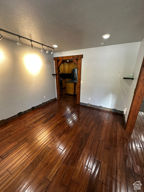 Unfurnished living room featuring a textured ceiling, baseboards, dark wood finished floors, and rail lighting