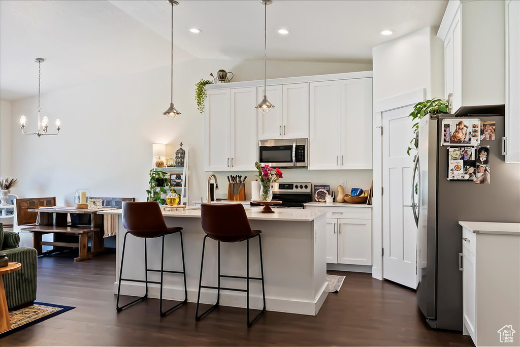 Kitchen featuring appliances with stainless steel finishes, lofted ceiling, dark wood-style floors, a kitchen breakfast bar, and white cabinets